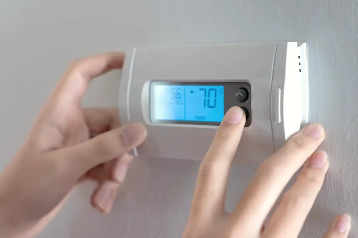 Hands adjusting a digital wall thermostat
